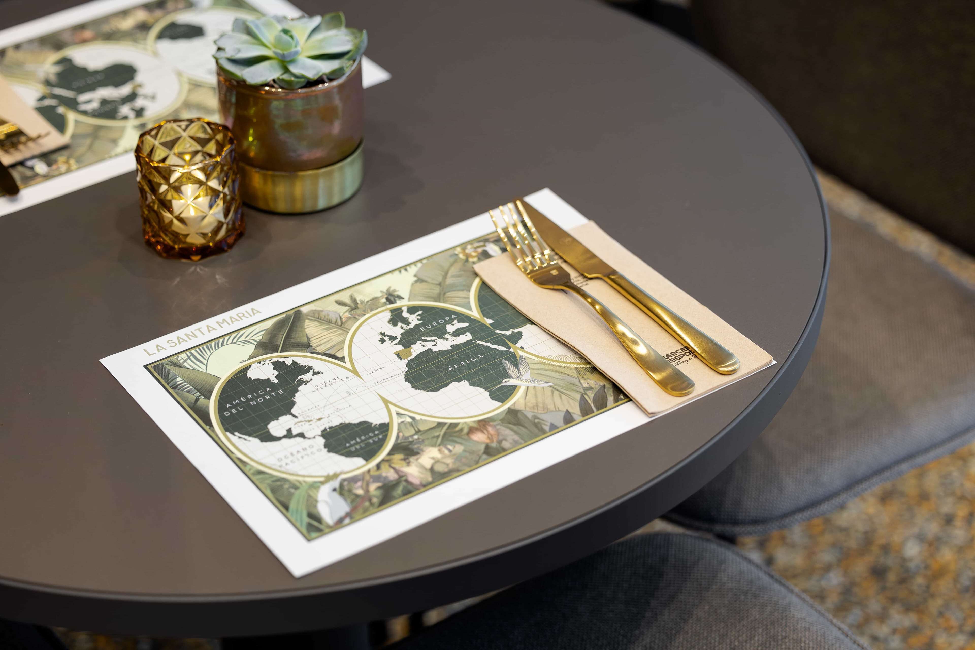 A table with a placemat featuring a world map, a gold fork and knife, and a decorative candle.