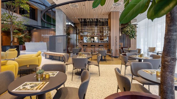 Un hall d’hôtel moderne avec un bar central, des espaces aménagés pour s’asseoir et un escalier bien visible.