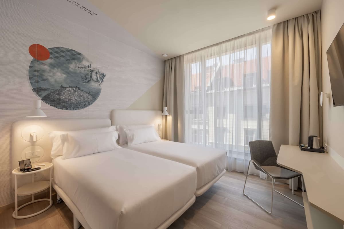 Ein Hotelzimmer mit zwei Betten, einem Schreibtisch, einem Stuhl, einer Lampe und einem großen Wandbild.
