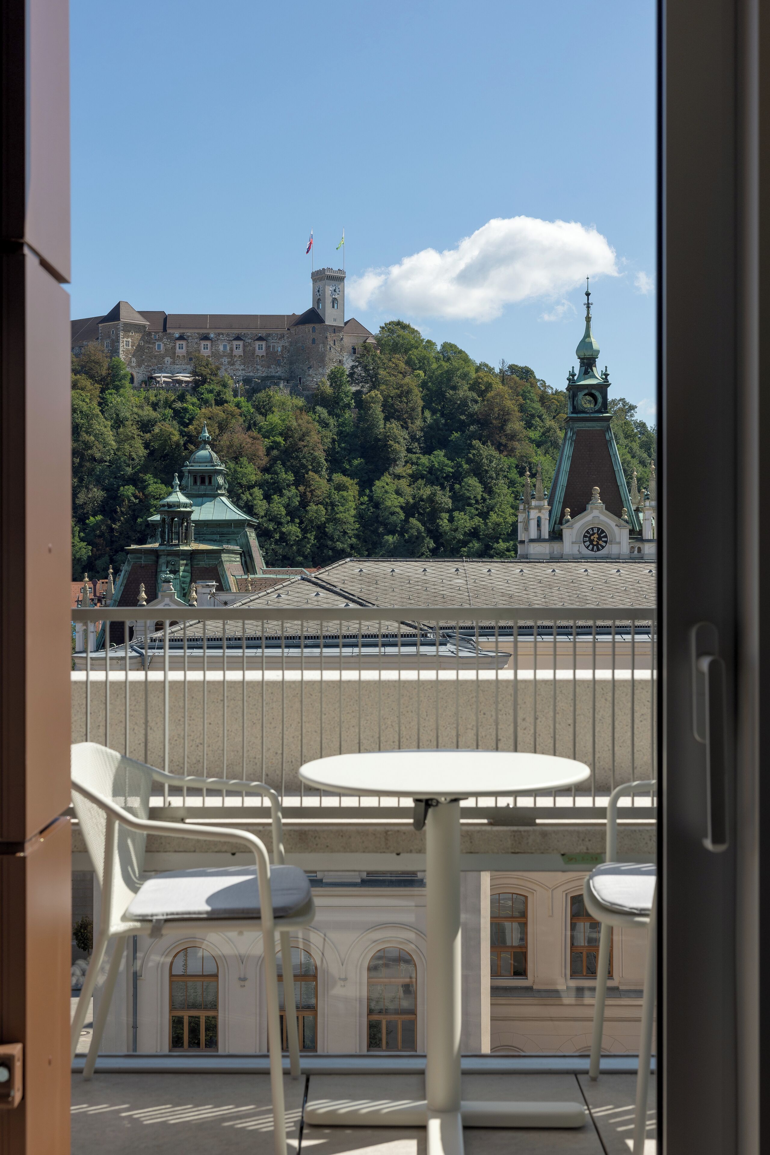A balcony with a view of a historic building with a clock tower and a church with a green roof.