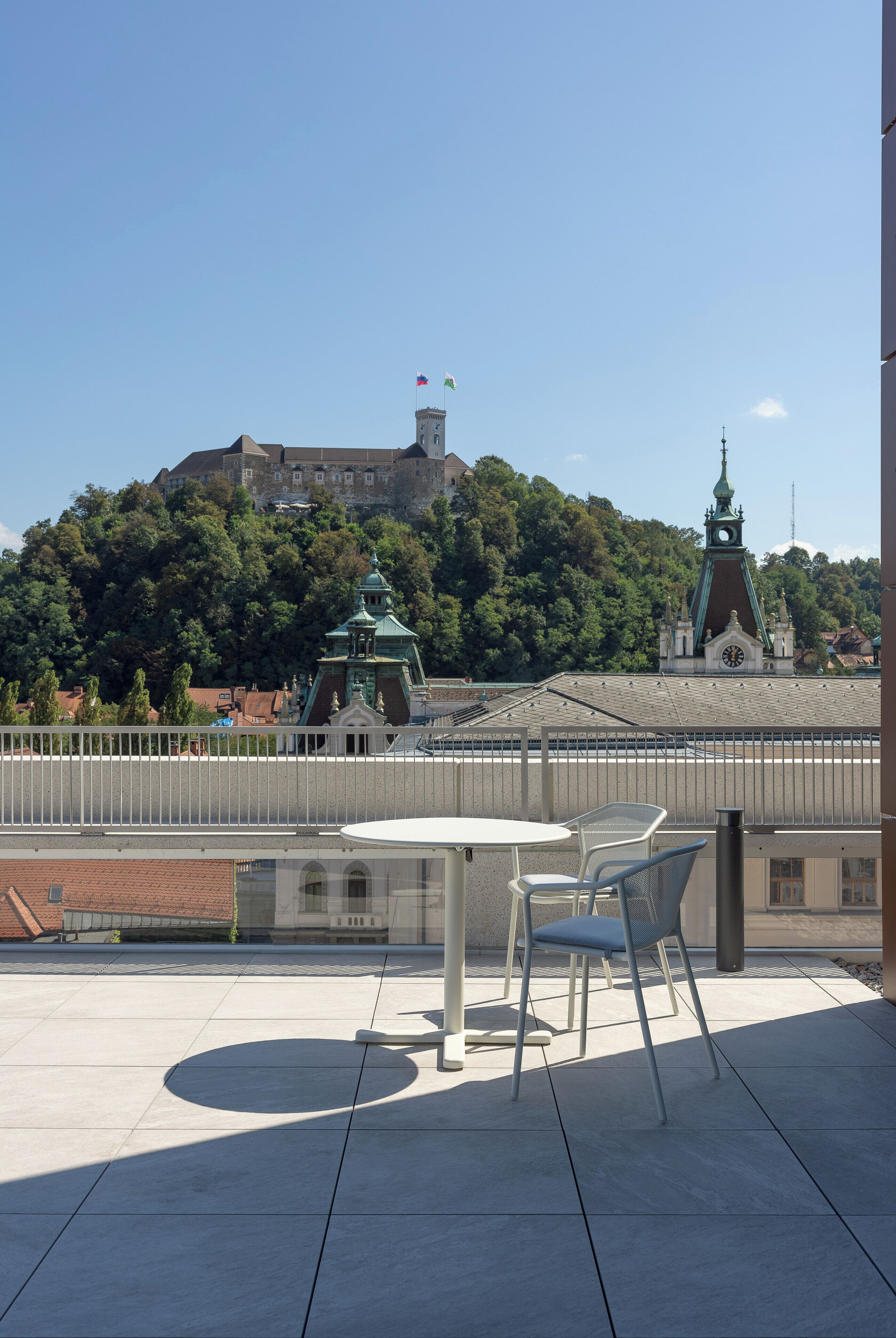 Una terrazza con tavolo e sedie, con vista su un edificio storico con una torre dell'orologio e una chiesa su una collina.