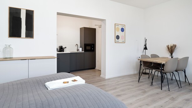 A modern room with a bed, a dining table with chairs, a kitchen area, and a wall-mounted artwork. - nestup Hildesheim Zentral (Hildesheim)
