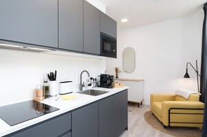 Cocina moderna con armarios grises, microondas y pileta. Hay un sillón amarillo y una pequeña mesa con una lámpara.