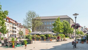 An outdoor café area with tables and chairs, surrounded by potted plants and umbrellas. - nestup Hildesheim Zentral (Hildesheim)