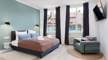 Ein modernes Schlafzimmer mit Bett, Nachttischen, einem Fernseher und Blick auf Gebäude.
