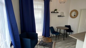 Una sala moderna con cortinas azules, una mesa redonda, dos sillas, un sofá azul y una pequeña mesa de centro de madera.