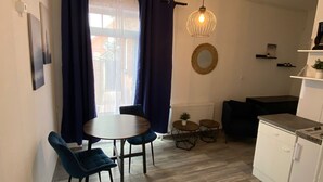 Cocina compacta con zona de comedor, que incluye una mesa redonda, dos sillas, una lámpara colgante y vistas a través de una ventana con cortinas.