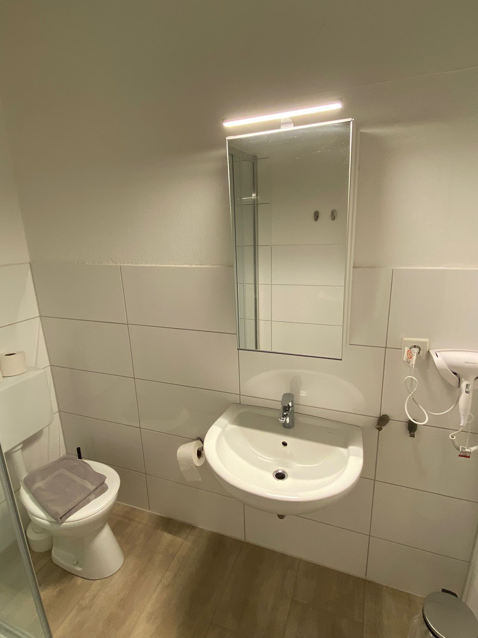 Ein Badezimmer mit weißem Waschbecken, Spiegel, Toilette und einem Föhn an der Wand.