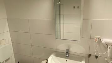 Ein Badezimmer mit weißem Waschbecken, Spiegel, Toilette und einem Föhn an der Wand.