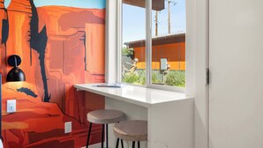 Una cucina moderna con un piano di lavoro bianco, due sgabelli da bar e un murale raffigurante un paesaggio desertico.