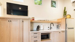 A modern kitchen with wooden cabinets, a built-in microwave, a stainless steel refrigerator, and a flat-screen TV mounted above the counter. - Downtown Moab • Hot Tub • Walk to Dining & Trails (Moab)