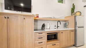 Eine moderne Küche mit Holzausstattung, einer eingebauten Mikrowelle, einem Edelstahlkühlschrank und einem flachbildfernseher, der über der Arbeitsfläche angebracht ist.