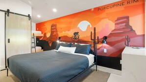 Ein modernes Schlafzimmer mit einem Bett, einem Schreibtisch und einem Wandgemälde einer Wüstenlandschaft.