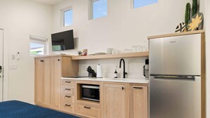 Una cucina compatta con mobili in legno, forno a microonde integrato, frigorifero in acciaio inossidabile e televisore a schermo piatto sopra il bancone.