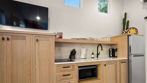 Ett modernt kök med träskåp, en inbyggd mikrovågsugn, ett kylskåp i rostfritt stål och en platt-TV som är monterad ovanför bänkskivan.