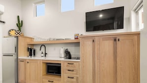 Ett modernt kök med träskåp, en inbyggd ugn, ett kylskåp, en kaffemaskin och en platt-TV som är monterad ovanför bänkskivan.