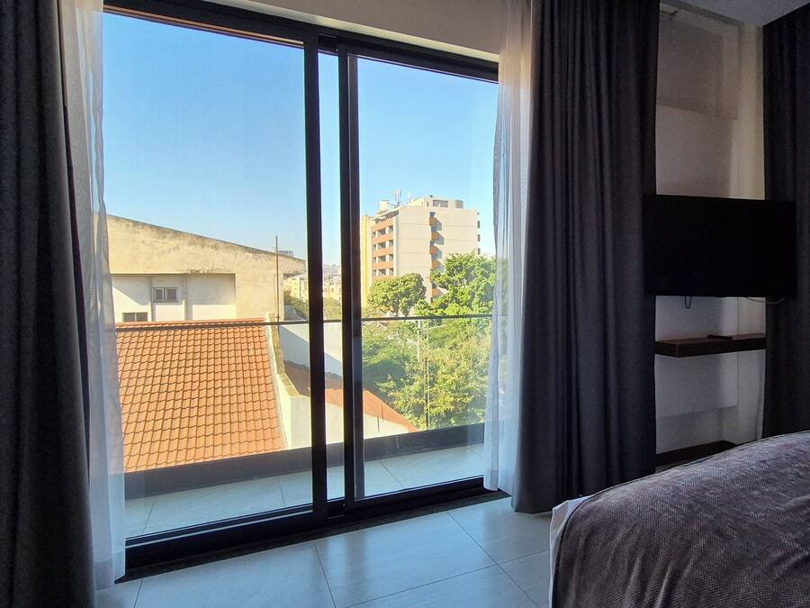 A hotel room with a large window, a bed, a TV mounted on the wall, and a balcony.