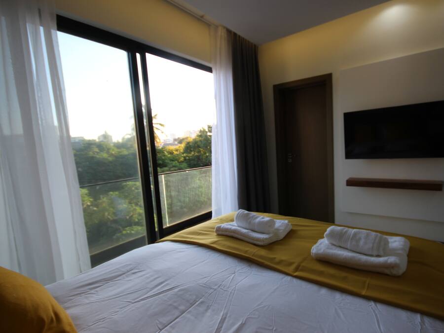 Une chambre d’hôtel avec un grand lit, un téléviseur fixé au mur et un balcon donnant sur un paysage verdoyant.