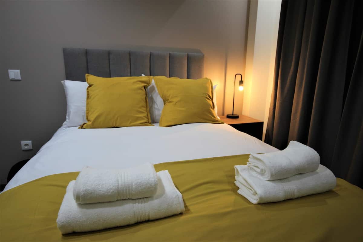 A neatly made bed with white and yellow bedding, a grey headboard, and a bedside lamp.