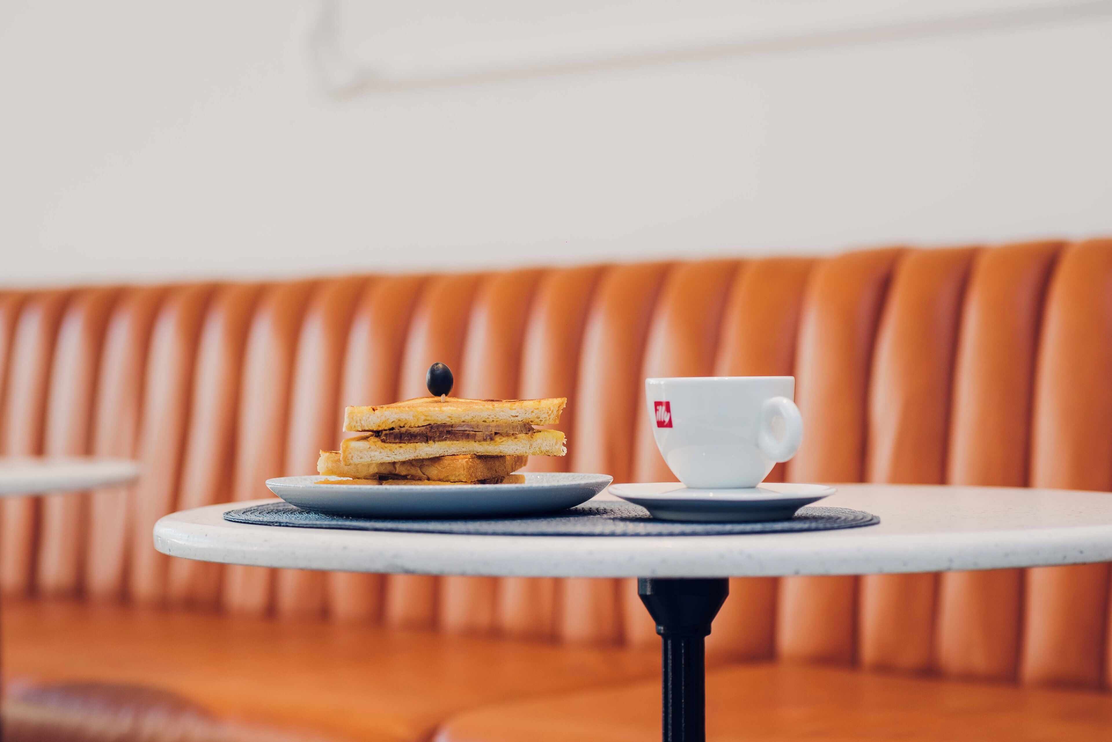 Ein runder Tisch mit einem Sandwich und einer Tasse auf einem weißen Untersetzer.