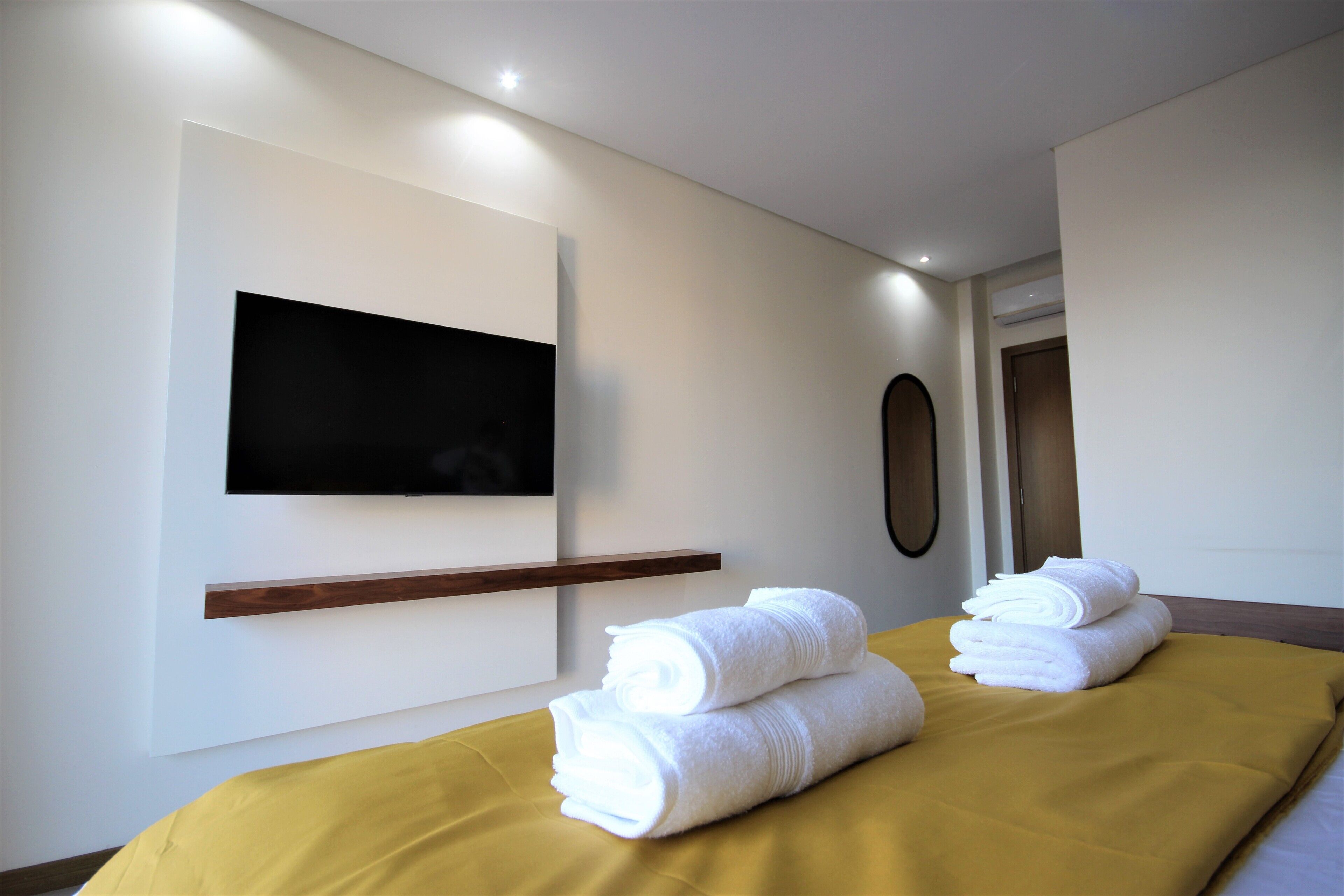 A hotel room with a bed, a flat-screen TV mounted on the wall, and a wooden shelf.