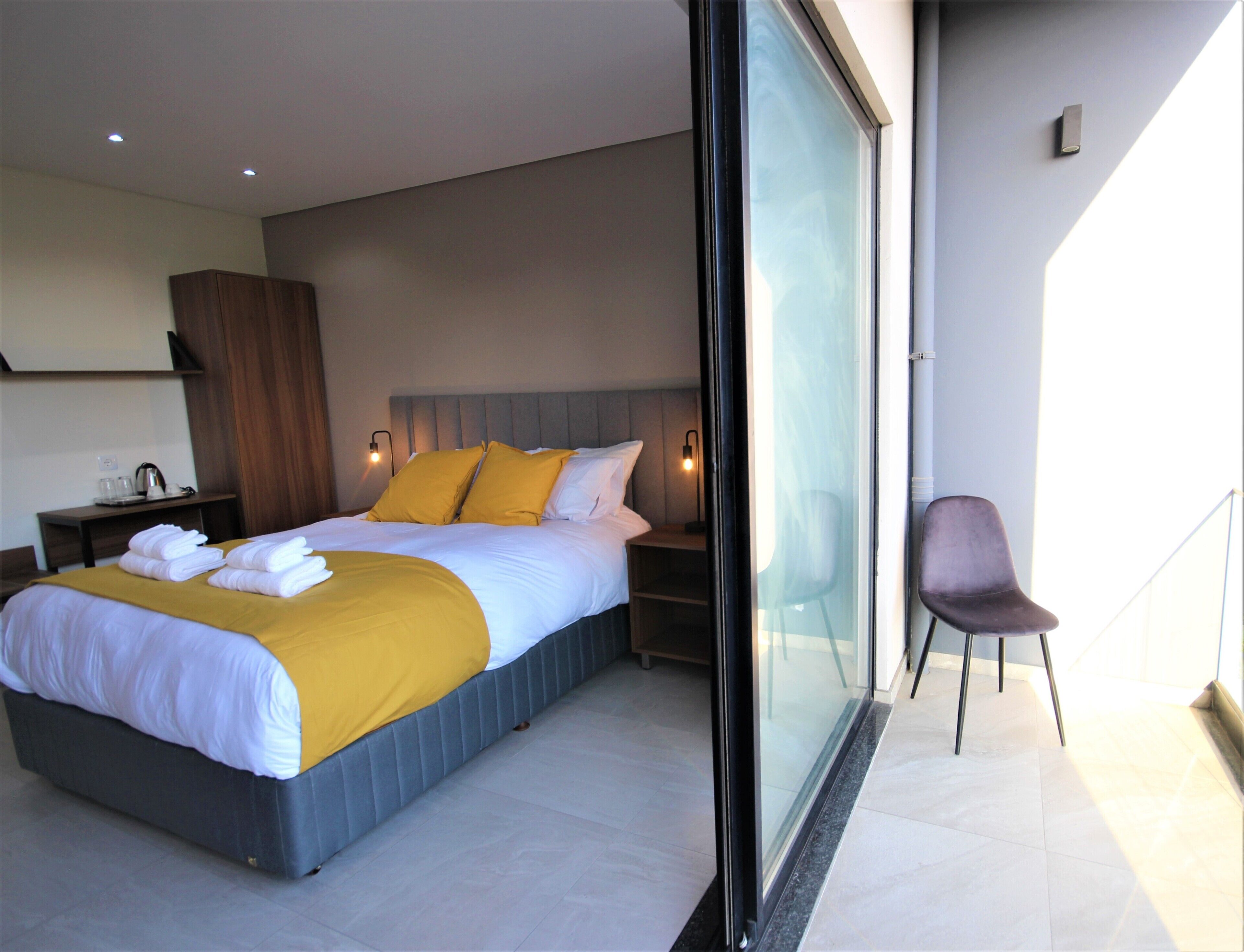 Una habitación de hotel moderna con una cama grande, una puerta de vidrio que da a un balcón y una silla.