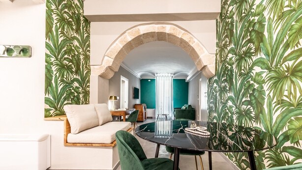 Una sala de estar moderna con una mesa redonda negra, sillas de terciopelo verde, un sofá beige y una pared de acento color aguamarina.