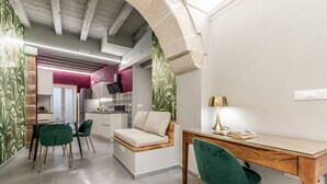 Una cocina moderna con horno integrado, un comedor con mesa de madera y sillas verdes, y una zona de estar acogedora con sofá.