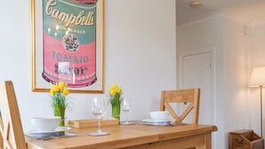 A dining area with a wooden table, chairs, and a framed picture of Campbell's Tomato Soup can.
