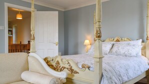 A bedroom with a four-poster bed, a sofa, and a door leading to another room.