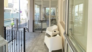 A balcony with a view of the water and buildings, a white chair, a small table, and a glass door leading to an indoor area. - bed and book (Rimini)