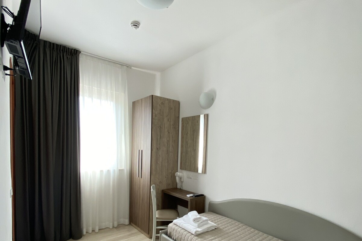 A modern bedroom with a bed, a wooden wardrobe, a desk, and a mirror.