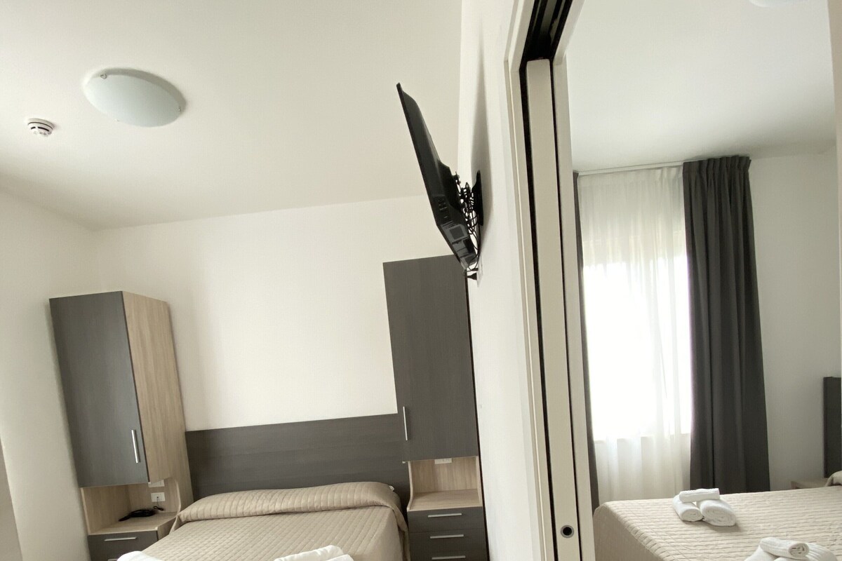 A hotel room with two beds, a wardrobe, a desk, and a mirror.