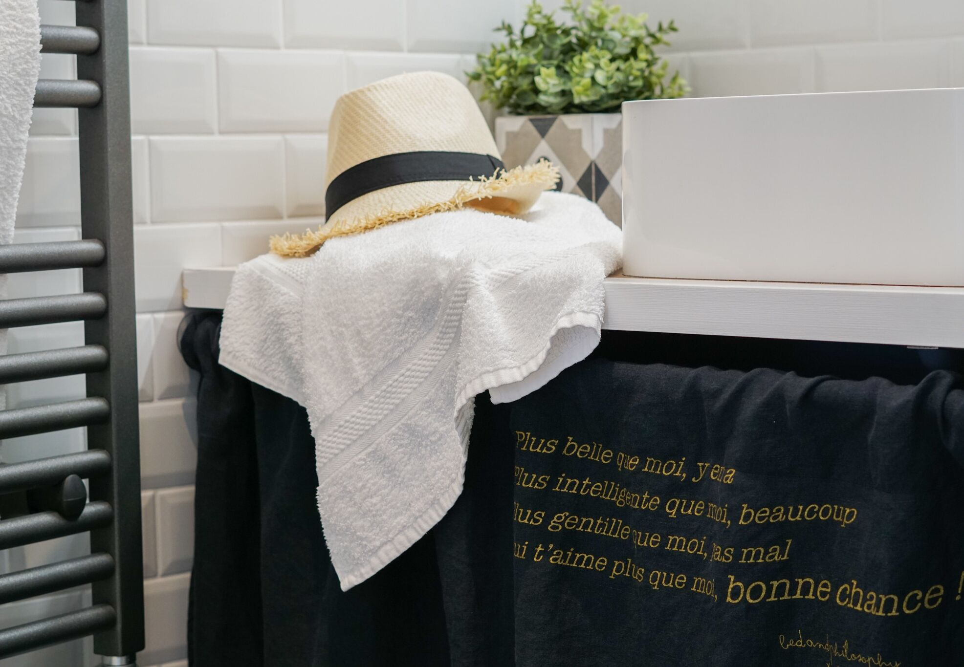 A towel and a black bag with French text on a white tiled wall.