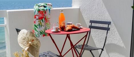 A balcony with a table and chair, a bottle of orange juice, and a bag with the Mariette logo.