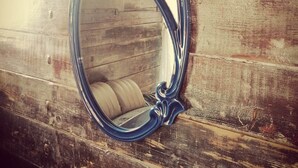 Un miroir avec un cadre orné, accroché à un mur en bois.