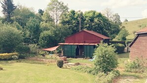 Une maison de campagne avec un toit rouge et des murs verts, entourée d’une cour verdoyante et d’arbres.