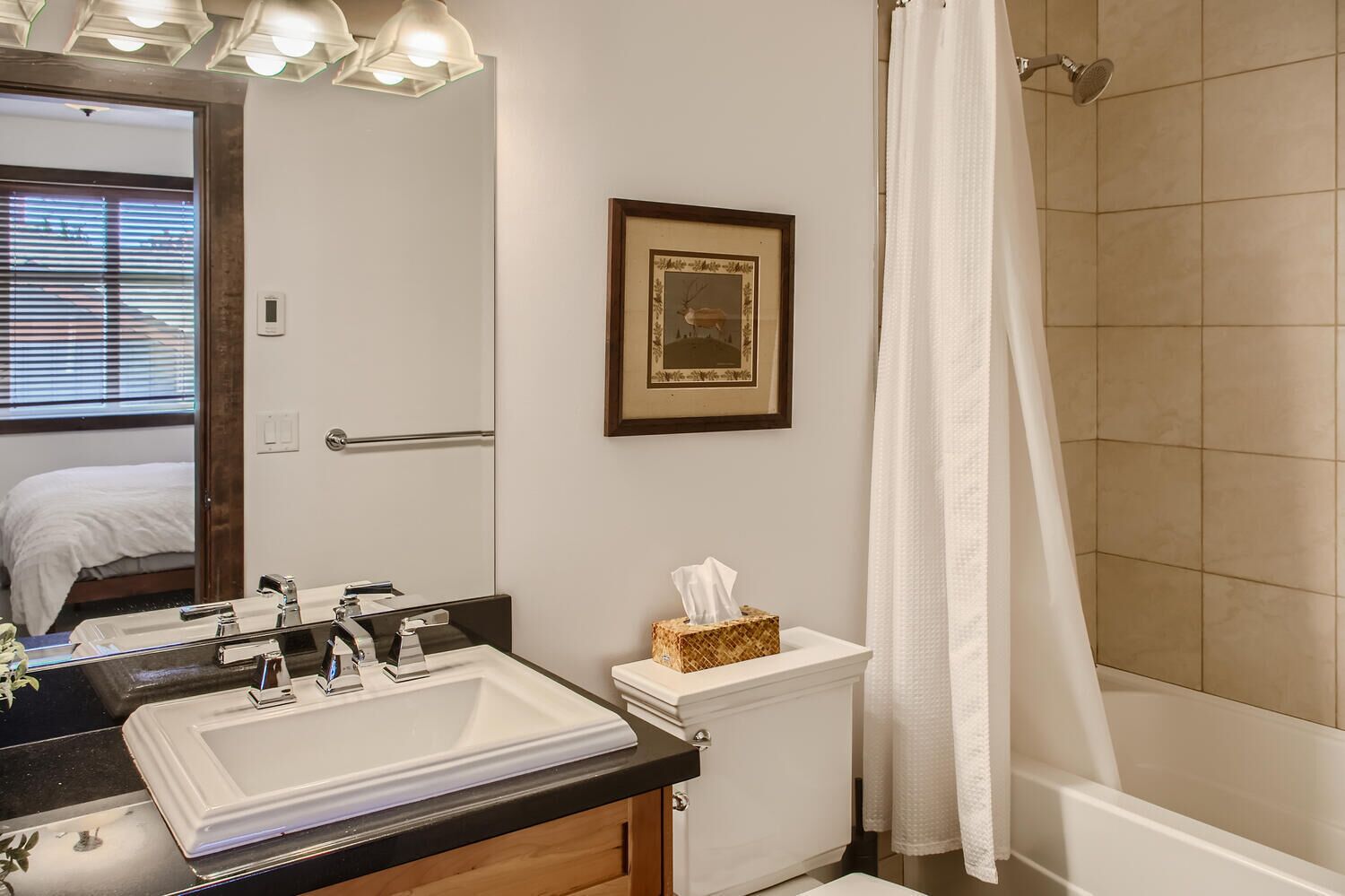 Une salle de bain avec un double lavabo, un tableau encadré au mur, des toilettes avec un porte-mouchoirs et un rideau de douche.