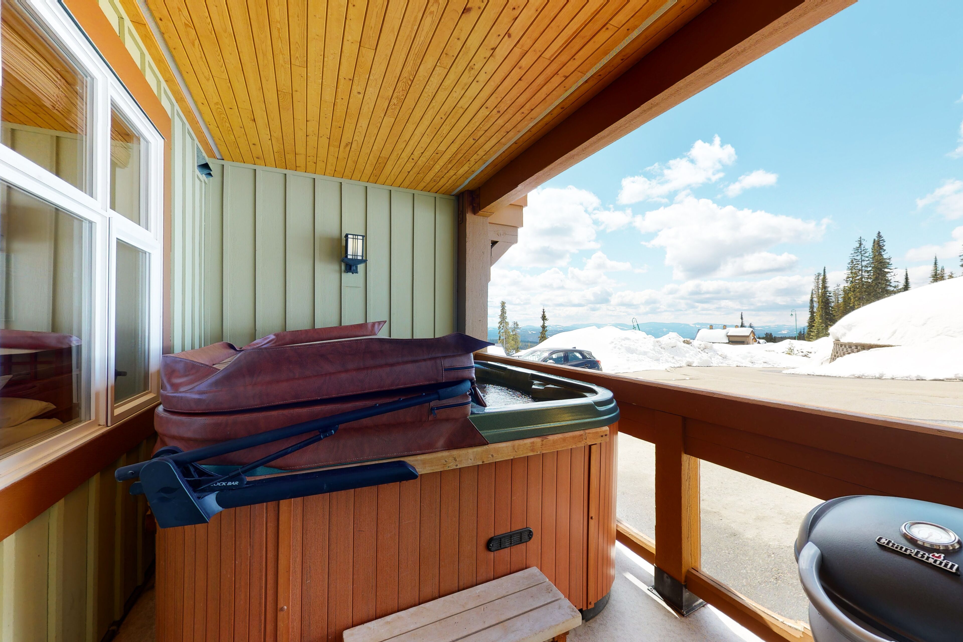 Una terraza de madera con un jacuzzi, un banco y vistas a un paisaje nevado.