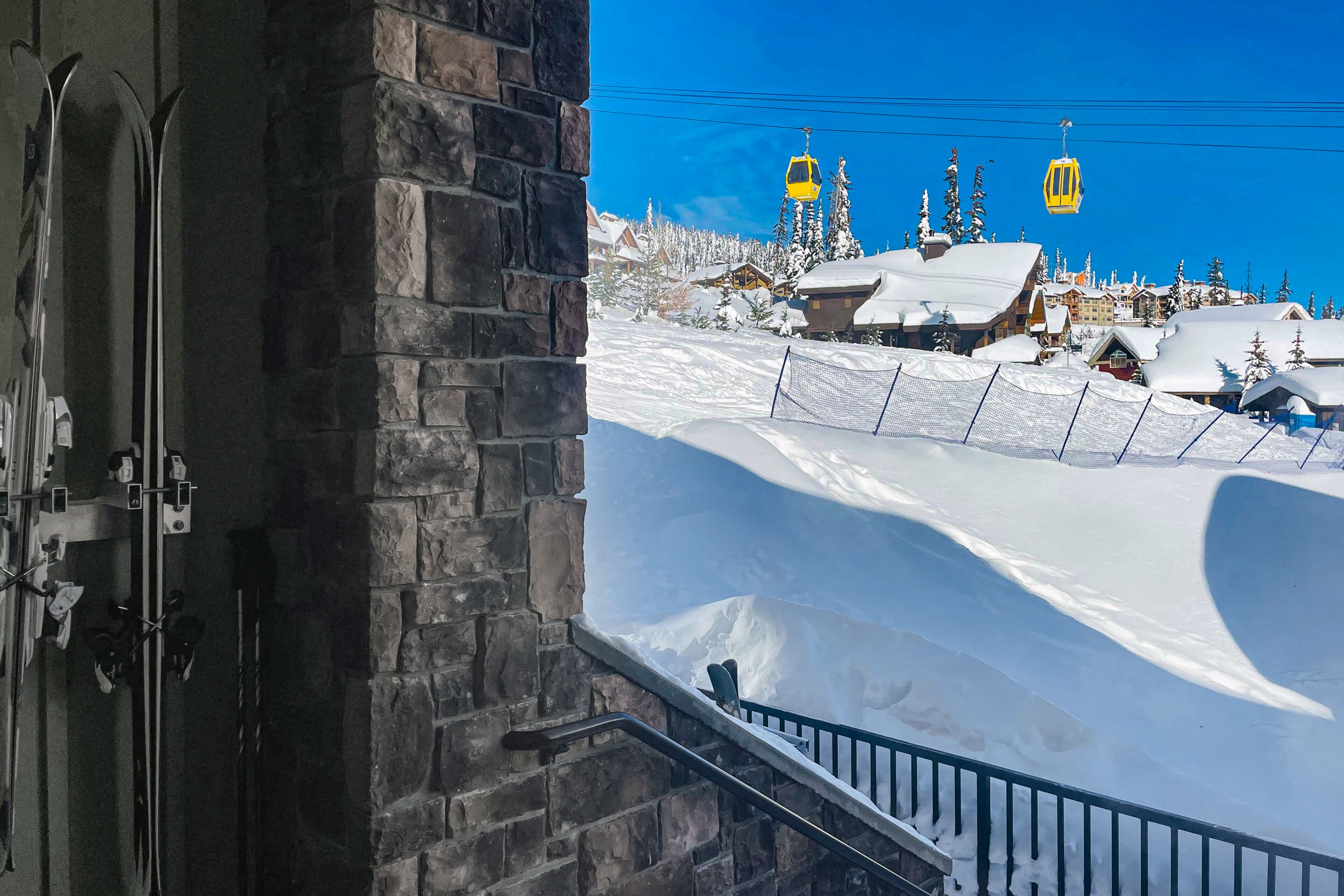 A ski lift chair suspended above a snowy landscape with buildings and trees in the background.