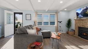 Una sala de estar con un sofá gris, una pequeña mesa de madera, una chimenea y una amplia pantalla de televisión.
