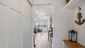 Un pasillo que conduce a una sala de estar con vista al mar, un banco de madera y un adorno de ancla en la pared.