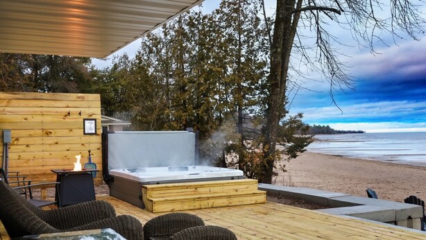 Una terraza de madera con mobiliario exterior, un jacuzzi y vista a la playa.