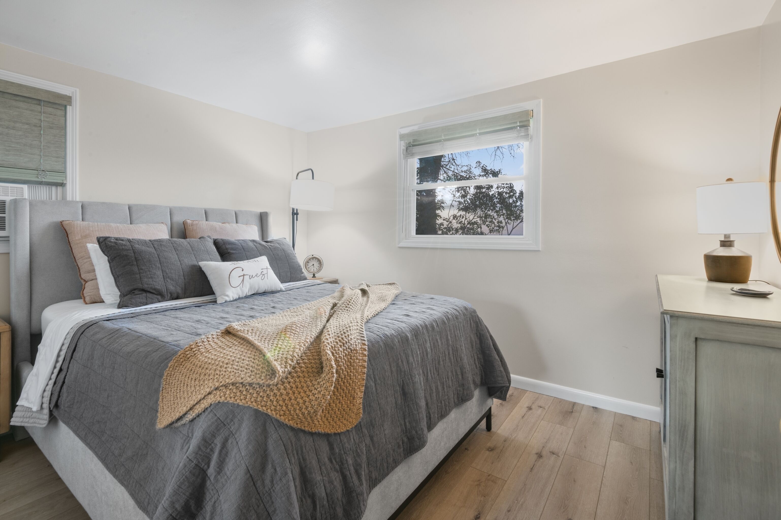Une chambre à coucher avec un lit, une table de chevet, une lampe et une fenêtre donnant sur des arbres.