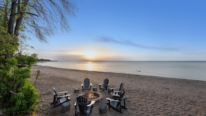 Una playa con un pozo de fuego y sillas Adirondack dispuestas para contemplar la puesta de sol.
