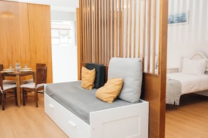 A compact room with a bed, a dining table with chairs, and a wooden partition.