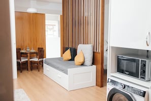 A compact room with a bed, a dining table, and a washing machine.