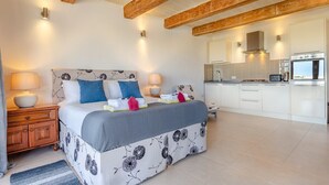 Een slaapkamer met een bed, nachtkastjes, een dressoir, een groot raam en een keukenhoek met een kookplaat en oven.