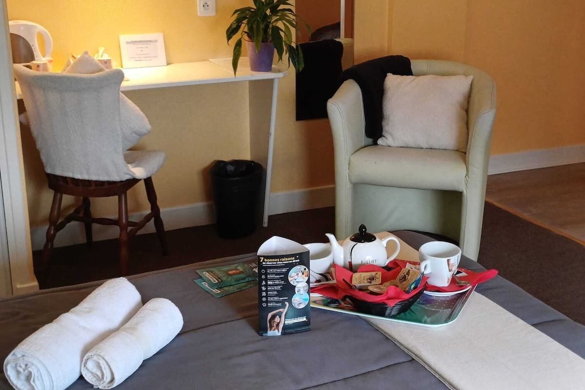 A hotel room with a desk, chair, and a seating area with a basket of tea and snacks.