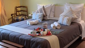 Una cama bien tendida con almohadas, una bandeja con alimentos para el desayuno y una silla en una habitación de hotel.